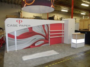 custom ecofriendly 10x10 trade show booth with overhead hanging banner, storage closet, product shelves and backlit display case