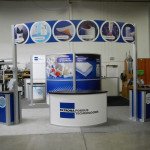 trade show booth island rental with meeting room kiosks workstations and large curved overhead banner