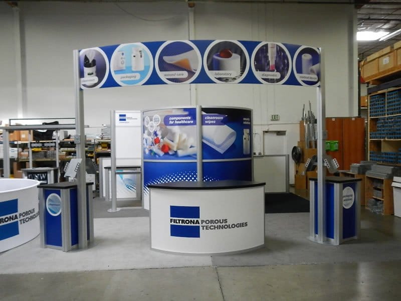 20x20 Trade Show Rental with conference room, product kiosk, work stations, and large curved header.